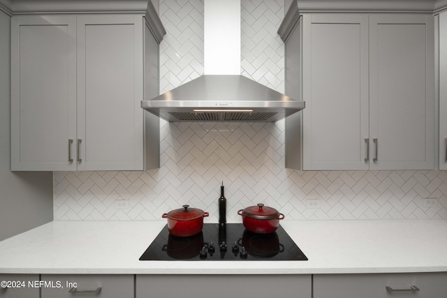 kitchen with backsplash, gray cabinets, black electric stovetop, and wall chimney range hood