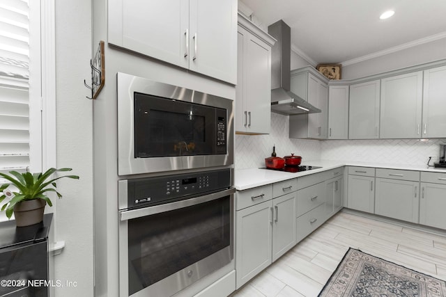 kitchen featuring stainless steel oven, black electric stovetop, wall chimney range hood, crown molding, and built in microwave