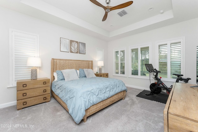 carpeted bedroom with a raised ceiling and ceiling fan