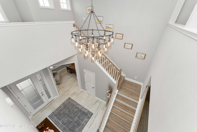 staircase with hardwood / wood-style flooring, a towering ceiling, and an inviting chandelier