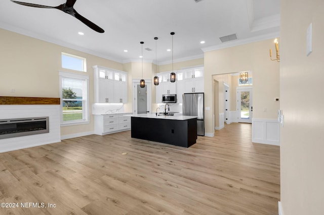 kitchen with white cabinets, stainless steel appliances, hanging light fixtures, and a kitchen island with sink