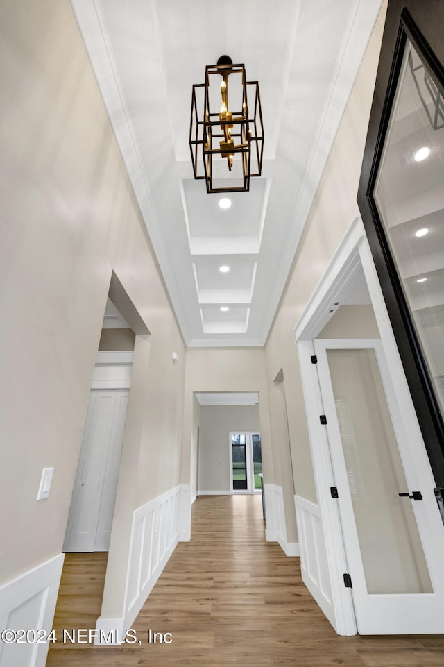 hall with crown molding, a towering ceiling, light hardwood / wood-style floors, and a notable chandelier