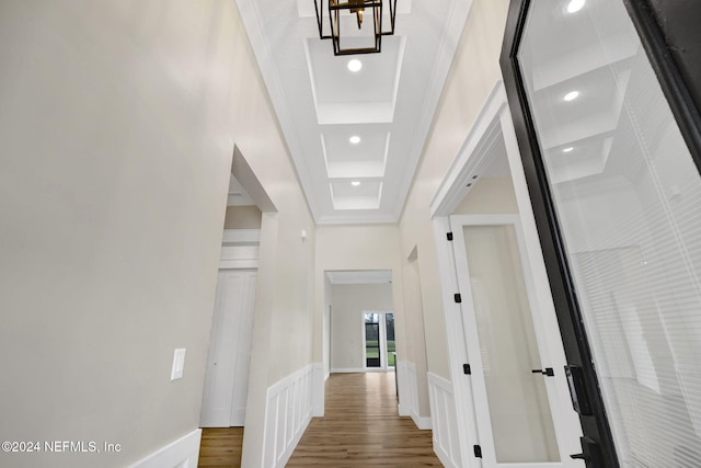 corridor with a raised ceiling, hardwood / wood-style floors, ornamental molding, and a notable chandelier