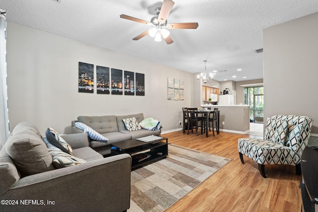 living room with ceiling fan with notable chandelier, wood-type flooring, and a textured ceiling