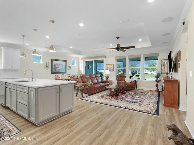 kitchen featuring ceiling fan, sink, hanging light fixtures, a center island with sink, and light wood-type flooring