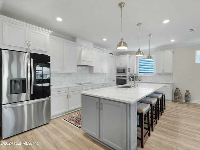 kitchen featuring appliances with stainless steel finishes, custom range hood, a kitchen island with sink, decorative light fixtures, and white cabinetry