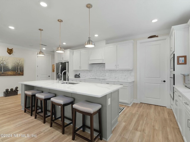 kitchen featuring white cabinets, hanging light fixtures, a kitchen island with sink, and custom exhaust hood