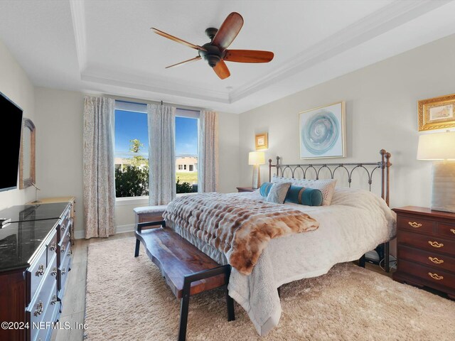 bedroom with ceiling fan, light wood-type flooring, crown molding, and a tray ceiling