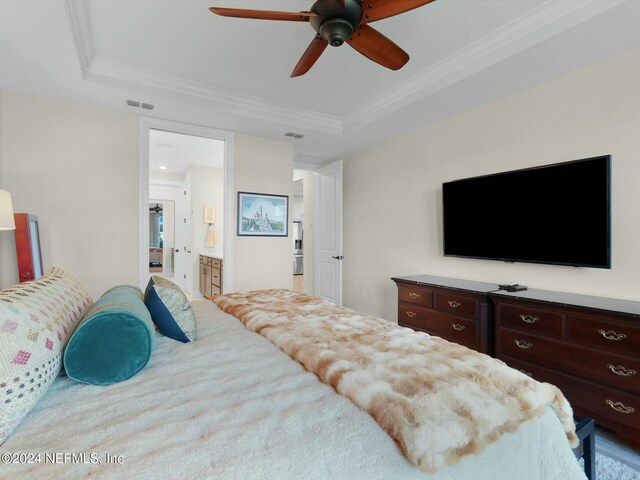 bedroom with a raised ceiling, ensuite bath, ceiling fan, and crown molding