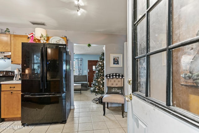 kitchen with black fridge, stove, light tile patterned floors, and extractor fan