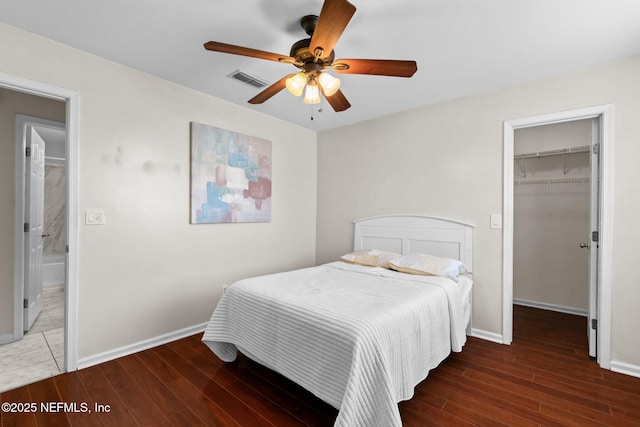 bedroom featuring dark wood-type flooring, a walk in closet, ceiling fan, and a closet