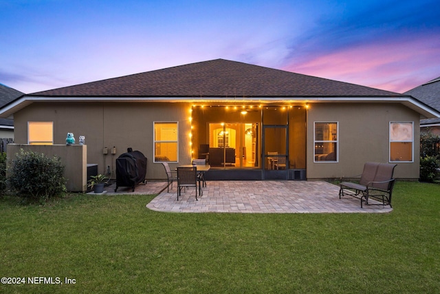 back house at dusk featuring a lawn and a patio area