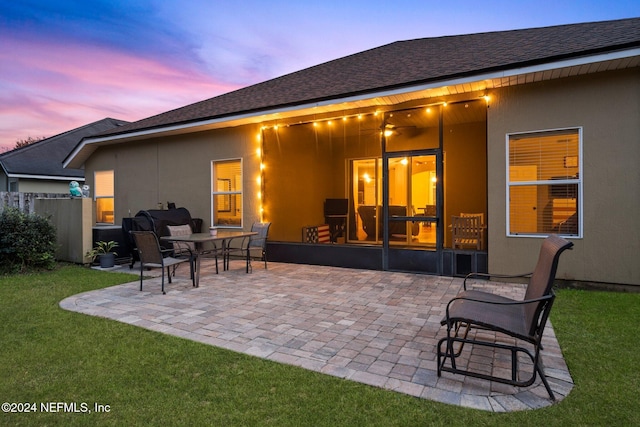 back house at dusk featuring a yard and a patio