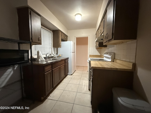 kitchen featuring stove, dark brown cabinetry, sink, light tile patterned floors, and white refrigerator