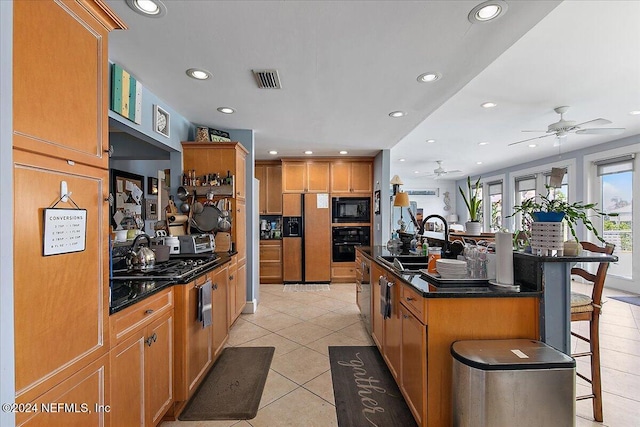 kitchen featuring sink, a kitchen breakfast bar, a center island with sink, light tile patterned flooring, and black appliances