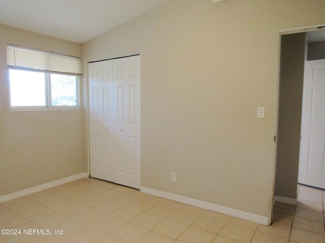 unfurnished bedroom featuring a closet, light tile patterned floors, and vaulted ceiling