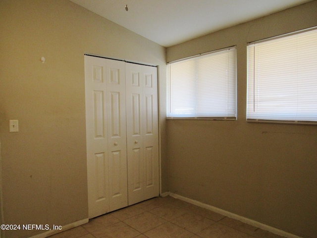 unfurnished bedroom with a closet, lofted ceiling, and tile patterned flooring