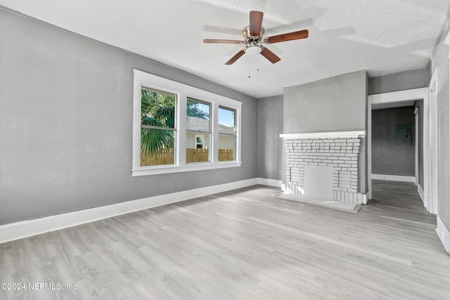 unfurnished room with a fireplace, ceiling fan, light hardwood / wood-style flooring, and a textured ceiling