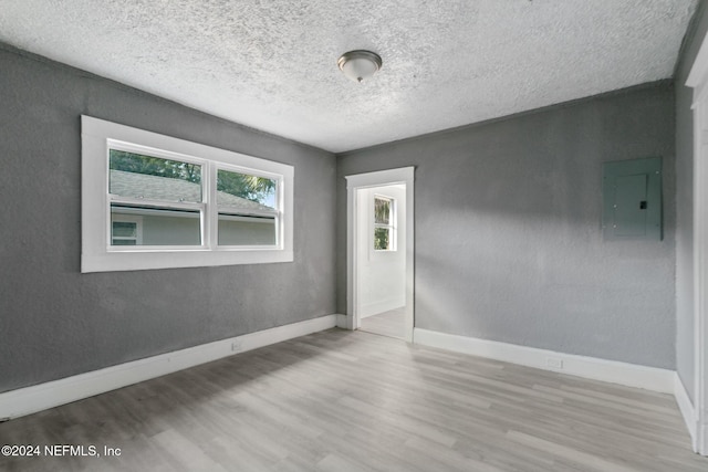 empty room featuring light wood-type flooring, a textured ceiling, and electric panel