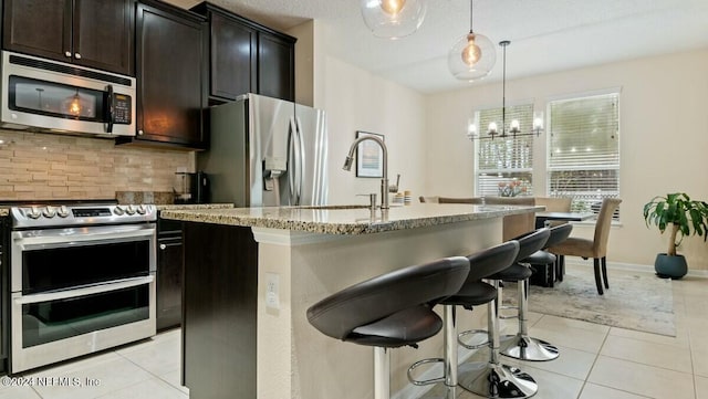 kitchen featuring decorative backsplash, decorative light fixtures, stainless steel appliances, and a center island with sink