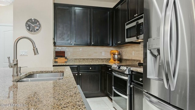 kitchen with light stone countertops, sink, stainless steel appliances, tasteful backsplash, and light tile patterned floors