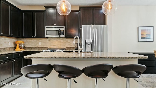 kitchen with a kitchen bar, appliances with stainless steel finishes, decorative backsplash, sink, and decorative light fixtures