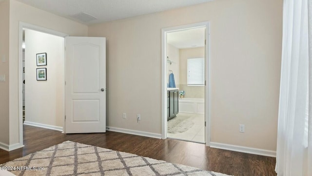 unfurnished bedroom featuring ensuite bath and dark wood-type flooring