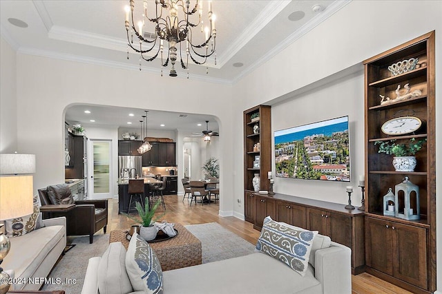 living room featuring light wood-type flooring, ceiling fan with notable chandelier, a tray ceiling, and crown molding