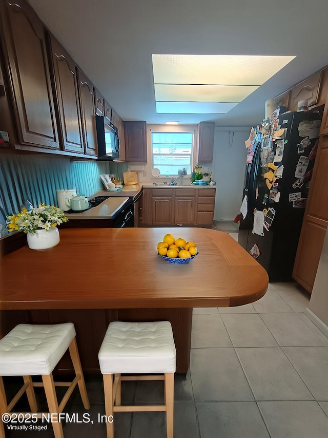 kitchen featuring light tile patterned floors, a kitchen breakfast bar, black appliances, and a peninsula