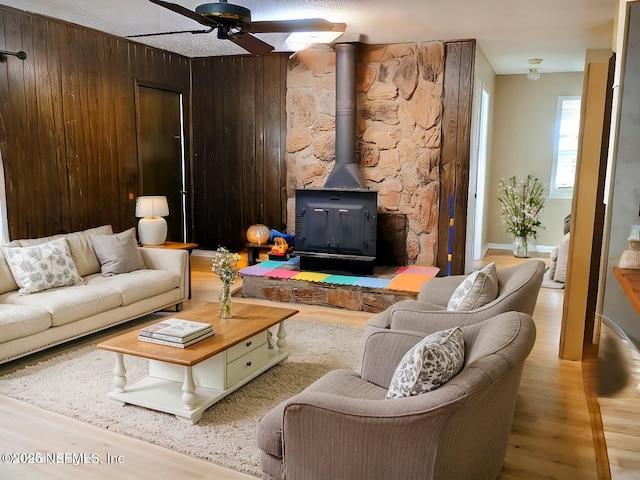 living room featuring wood walls, a wood stove, a ceiling fan, and wood finished floors