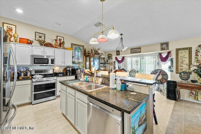 kitchen featuring stainless steel appliances, vaulted ceiling, white cabinetry, and an island with sink