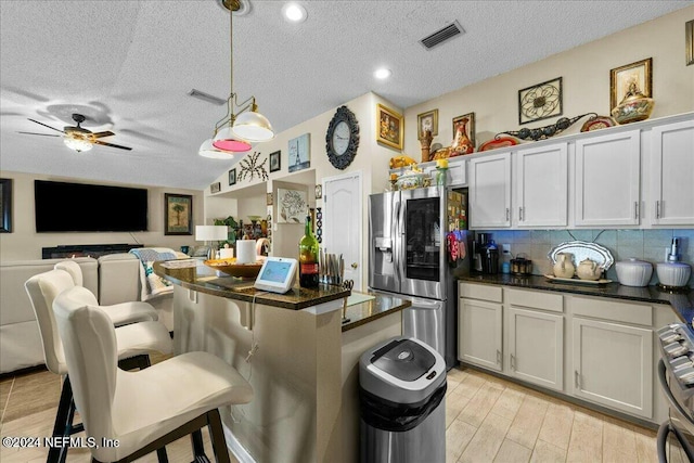 kitchen with stainless steel appliances, pendant lighting, a textured ceiling, a breakfast bar, and white cabinets