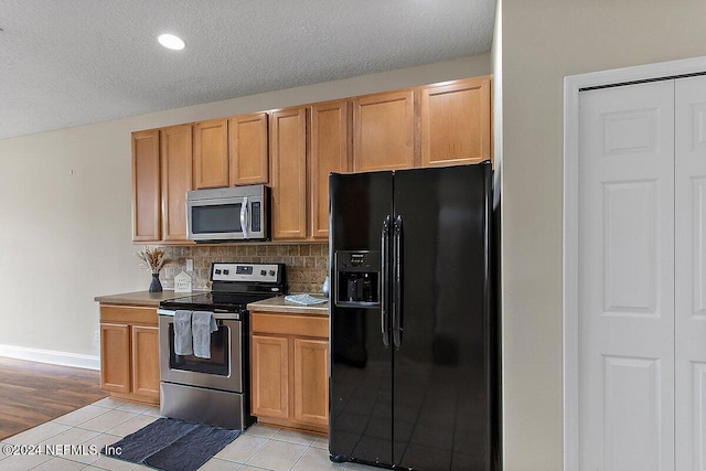 kitchen with backsplash, light tile patterned floors, stainless steel appliances, and a textured ceiling