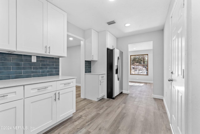 kitchen with stainless steel refrigerator with ice dispenser, tasteful backsplash, light stone counters, white cabinets, and light hardwood / wood-style floors