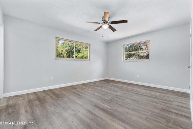 empty room featuring plenty of natural light, ceiling fan, light wood-type flooring, and a textured ceiling