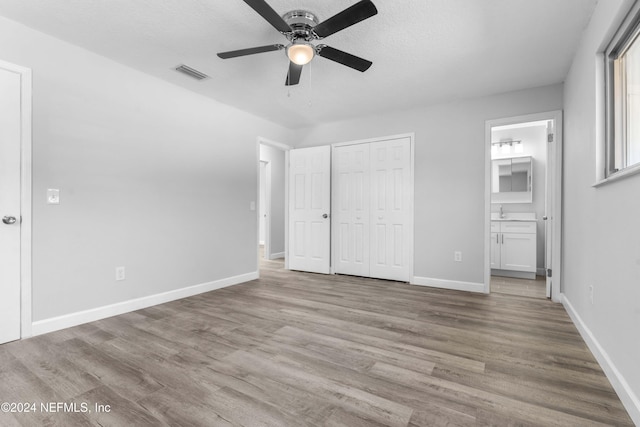 unfurnished bedroom featuring a textured ceiling, light hardwood / wood-style floors, ensuite bath, and ceiling fan