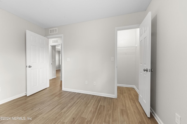 unfurnished bedroom featuring a closet, a spacious closet, and light hardwood / wood-style flooring