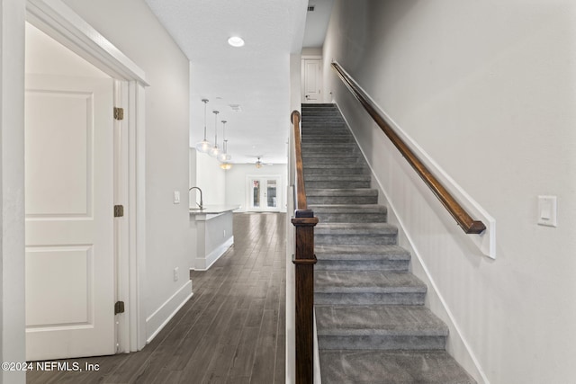 stairway featuring wood-type flooring, a textured ceiling, and sink