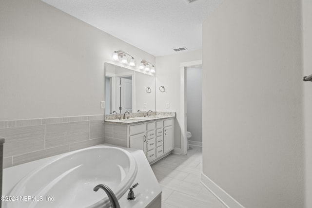 bathroom featuring a tub to relax in, tile patterned floors, a textured ceiling, toilet, and vanity