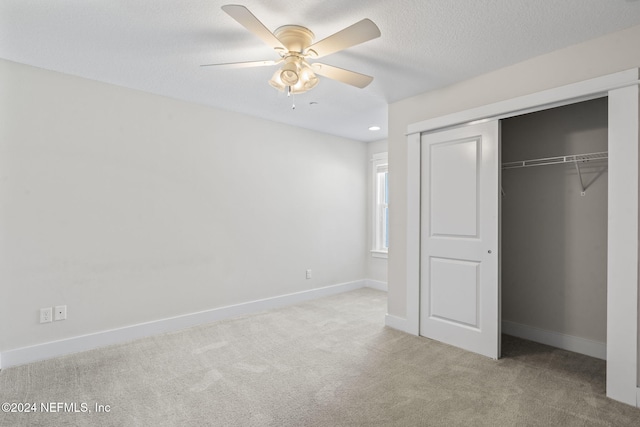 unfurnished bedroom with a textured ceiling, a closet, light colored carpet, and ceiling fan