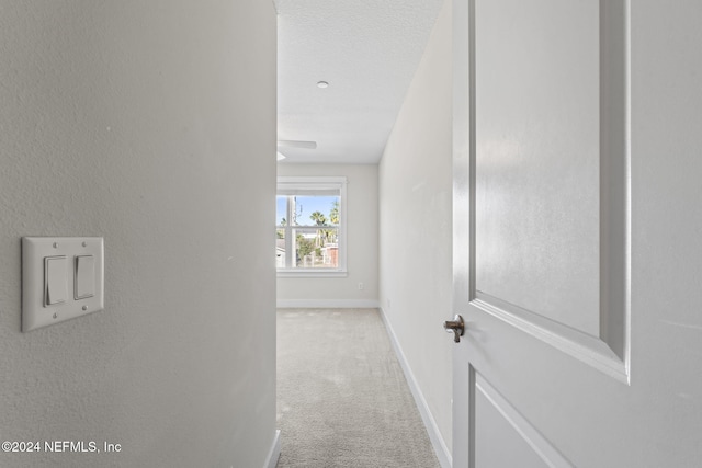 corridor featuring light colored carpet and a textured ceiling