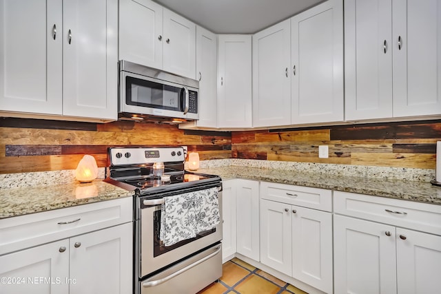 kitchen with light tile patterned flooring, light stone countertops, white cabinetry, and appliances with stainless steel finishes