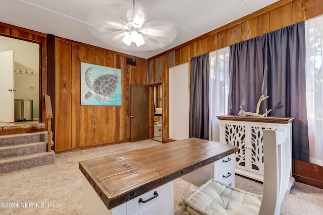 carpeted office space featuring ceiling fan and wood walls