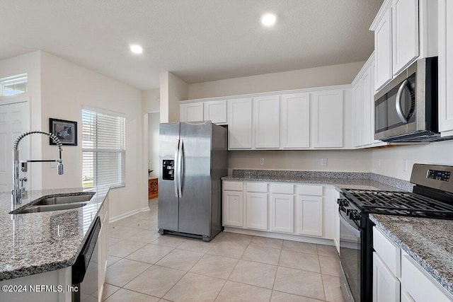 kitchen featuring sink, white cabinets, dark stone counters, light tile patterned flooring, and appliances with stainless steel finishes