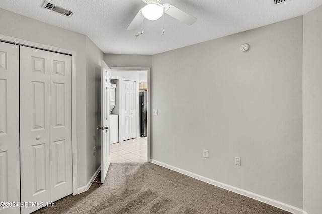 unfurnished bedroom with stainless steel fridge, a textured ceiling, light colored carpet, ceiling fan, and a closet