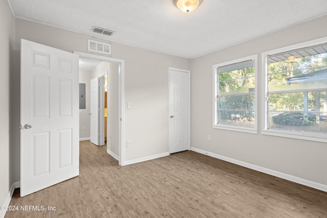 unfurnished bedroom featuring hardwood / wood-style floors, a textured ceiling, and electric panel