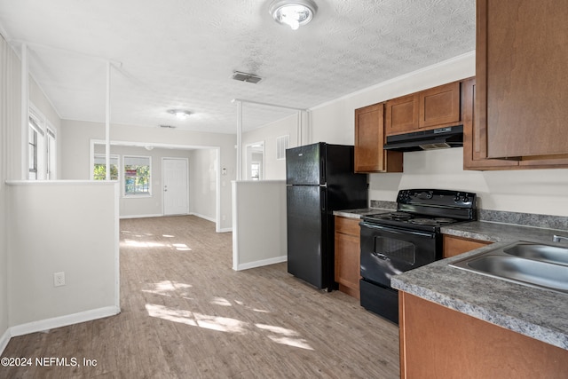 kitchen featuring light wood-type flooring, a textured ceiling, sink, black appliances, and hanging light fixtures