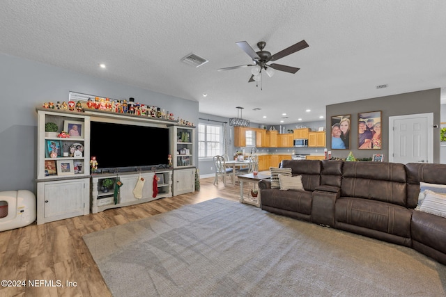 living room with a textured ceiling, light wood-type flooring, and ceiling fan