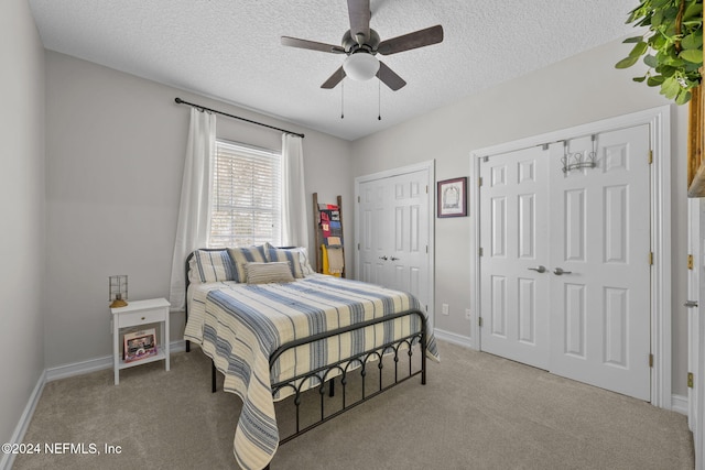 carpeted bedroom featuring a textured ceiling, ceiling fan, and multiple closets