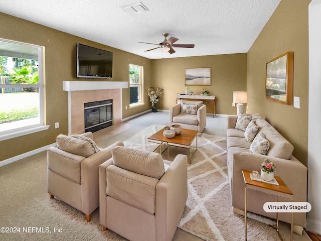 carpeted living room featuring a tile fireplace, a textured ceiling, a wealth of natural light, and ceiling fan